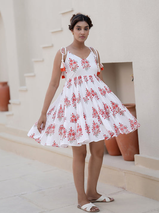 A woman standing near step wearing a white cotton short dress with red and black floral block prints and a floral head accessory.